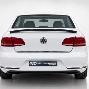 Rear view of a white Volkswagen sedan showing taillights, emblem, and a Motordrome Design plate on the bumper, in a studio setting