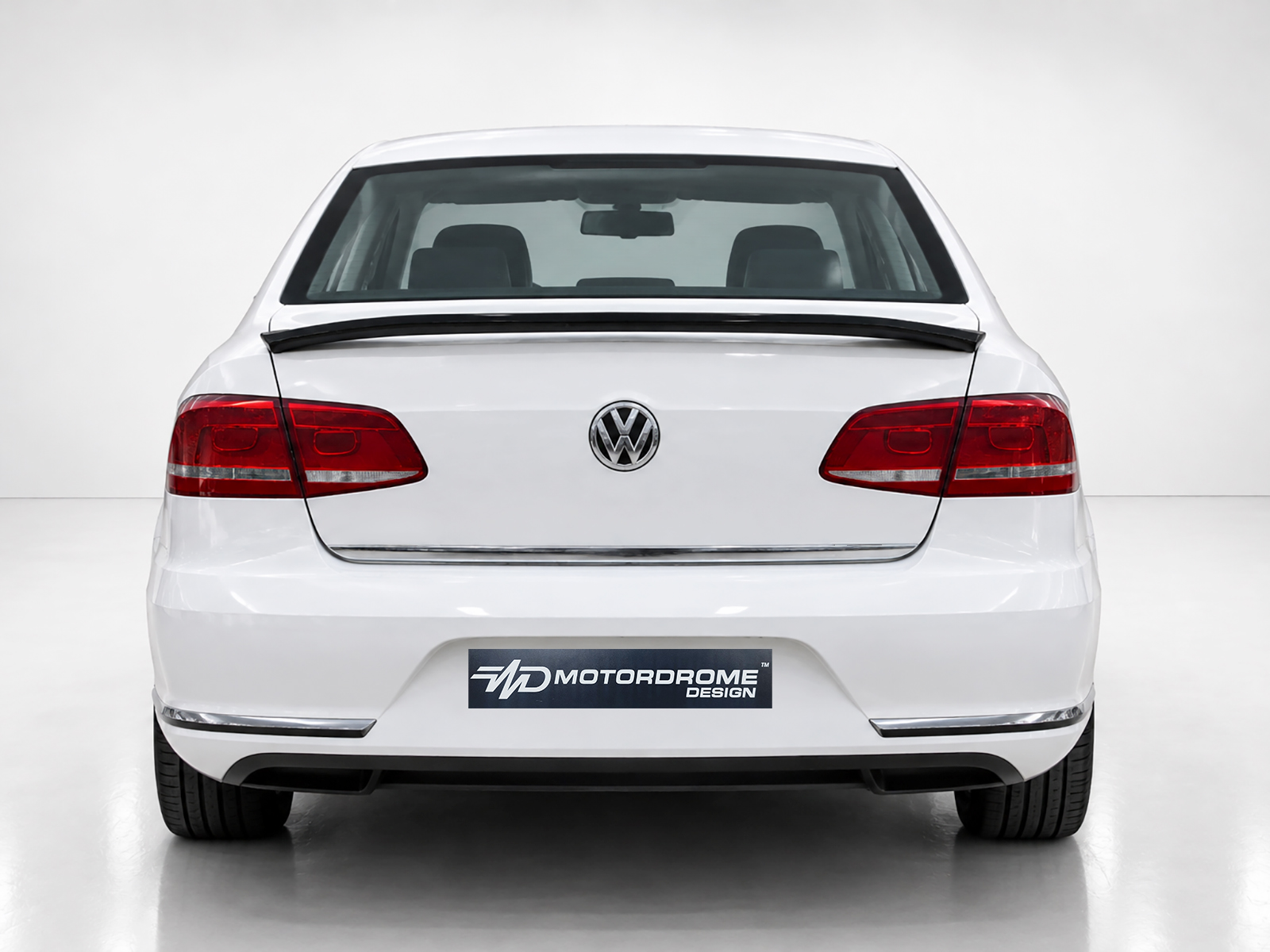 A-432_1jpg - OPSHOLDERS Rear view of a white Volkswagen sedan showing taillights, emblem, and a Motordrome Design plate on the bumper, in a studio setting
