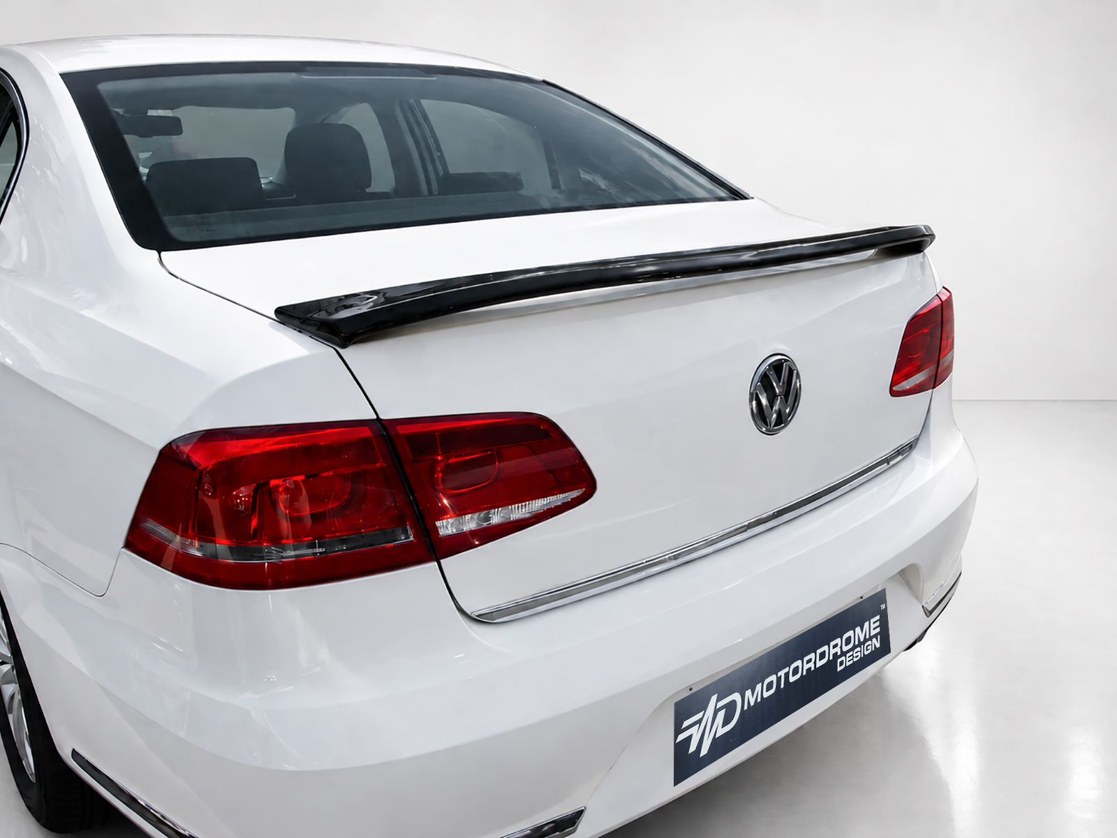 A-432_2jpg - OPSHOLDERS White Volkswagen sedan rear view with a black spoiler and red tail lights in a studio setting, logo visible on trunk badge