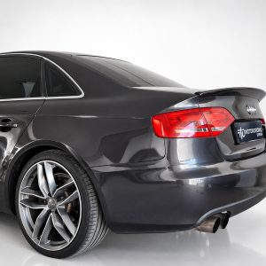 Rear three-quarter view of a dark gray Audi sedan with large alloy wheels in a studio setting.
