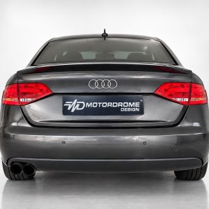 A-443_2jpg - OPSHOLDERS Rear view of a gray Audi sedan in a studio, showing taillights, dual exhausts, and a MOTORDROME DESIGN license plate.