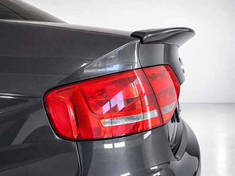 A-443_3jpg - OPSHOLDERS Rear end of a dark gray car showing the red tail light and rear spoiler in a studio setting