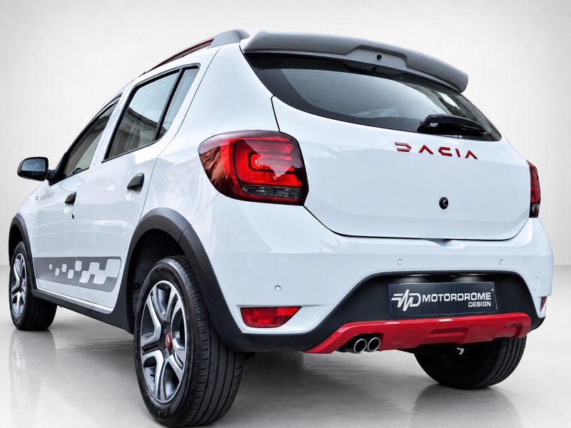 A-445_3jpg - OPSHOLDERS Rear three-quarter view of a white hatchback with red DACIA badge and Motordrome Design plate, indoors.