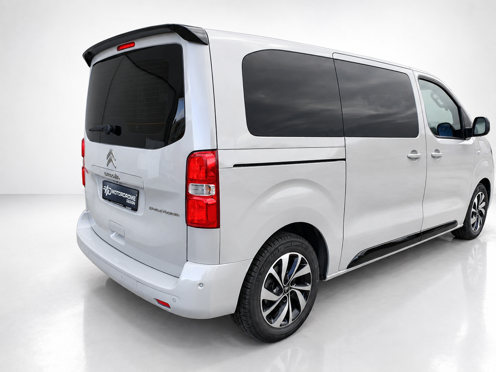 A-449_1jpg - OPSHOLDERS Rear three-quarter view of a white van with dark-tinted windows and alloy wheels, photographed in a bright studio setting.