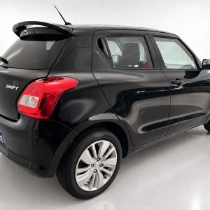 Rear three-quarter view of a black Suzuki Swift hatchback with red tail light and alloy wheels in a showroom setting