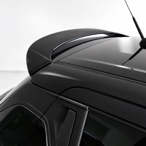 Close-up of a black car roof with a rear spoiler and antenna against a light background.
