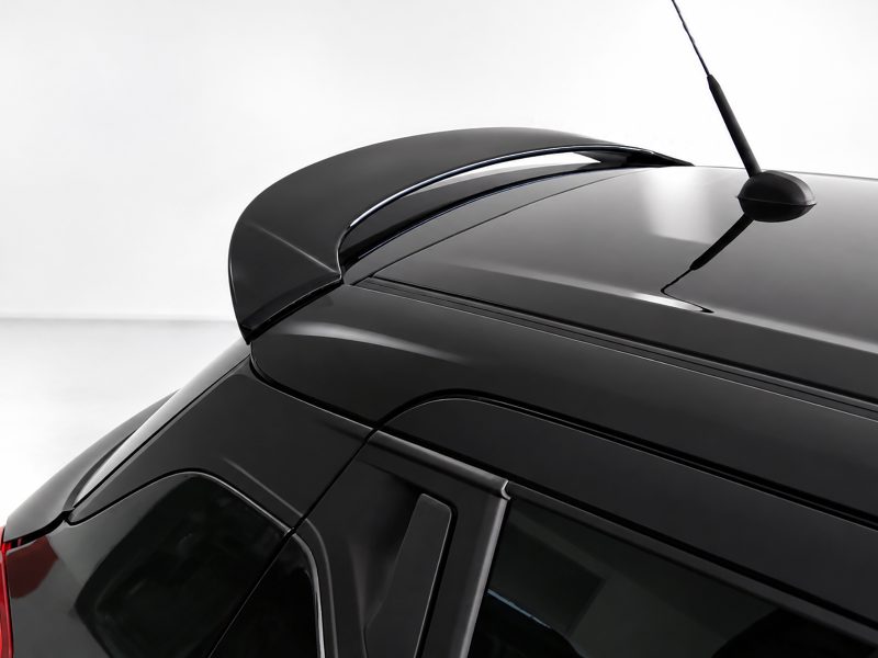 Close-up of a black car roof with a rear spoiler and antenna against a light background.