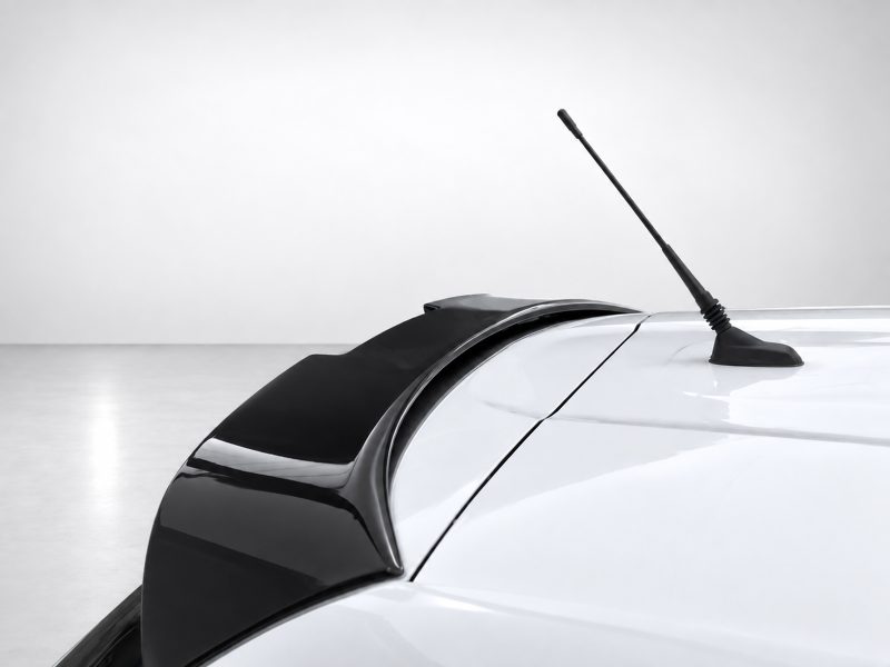 White car roof with a black whip antenna extending upward, seen from the rear side edge in a bright studio setting.