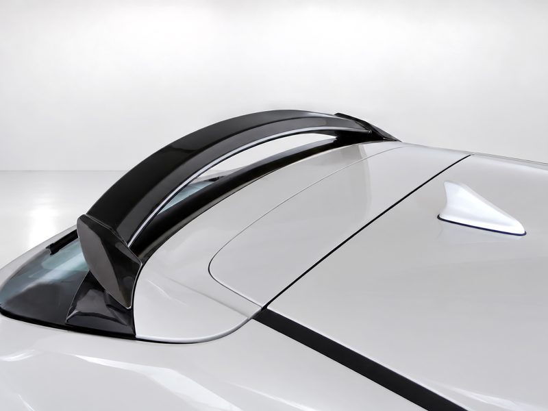 Close-up of a white sports car roof showing a black Targa-style bar and a shark-fin antenna on top.