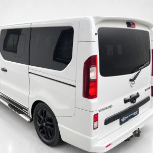 A-455_3jpg - OPSHOLDERS Rear-left view of a white Vivaro van with dark-tinted windows, black alloy wheels, and a rear spoiler.