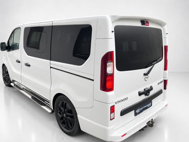 A-455_3jpg - OPSHOLDERS Rear-left view of a white Vivaro van with dark-tinted windows, black alloy wheels, and a rear spoiler.