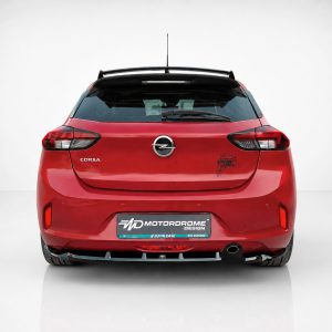 A-456_3jpg - OPSHOLDERS Rear view of a red Opel Corsa hatchback in a studio setting, with a Motordrome Design plate and a small decal on the right rear door.