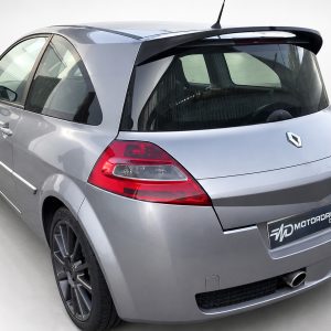 A-459_4jpg - OPSHOLDERS Rear three-quarter view of a silver Renault hatchback with large alloy wheels and red taillights, in a showroom setting (MOTORDROME plate).
