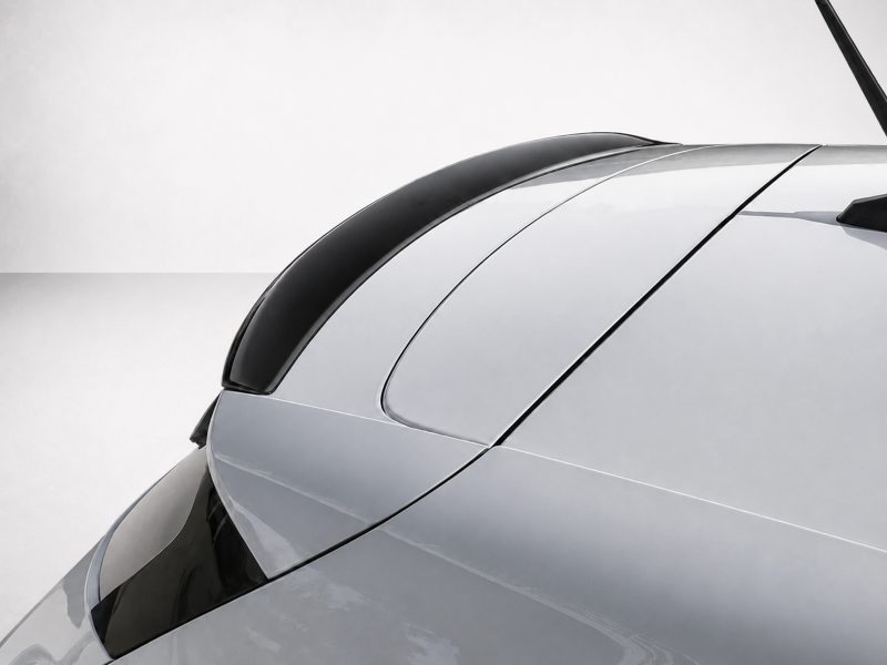 A-460_4jpg - OPSHOLDERS Close-up of a silver car hood with smooth, curved lines and a black roof trim against a pale background.