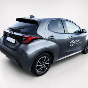 A-463_2jpg - OPSHOLDERS Rear three-quarter view of a gray Toyota Yaris hatchback with 'Yaris Why Stop?' branding on the side, in a studio setting.