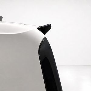 Close-up of a white car's rear corner showing a black spoiler and rear window against a light background.