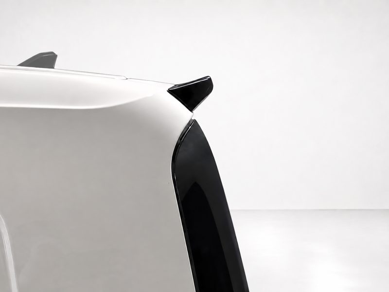 Close-up of a white car's rear corner showing a black spoiler and rear window against a light background.