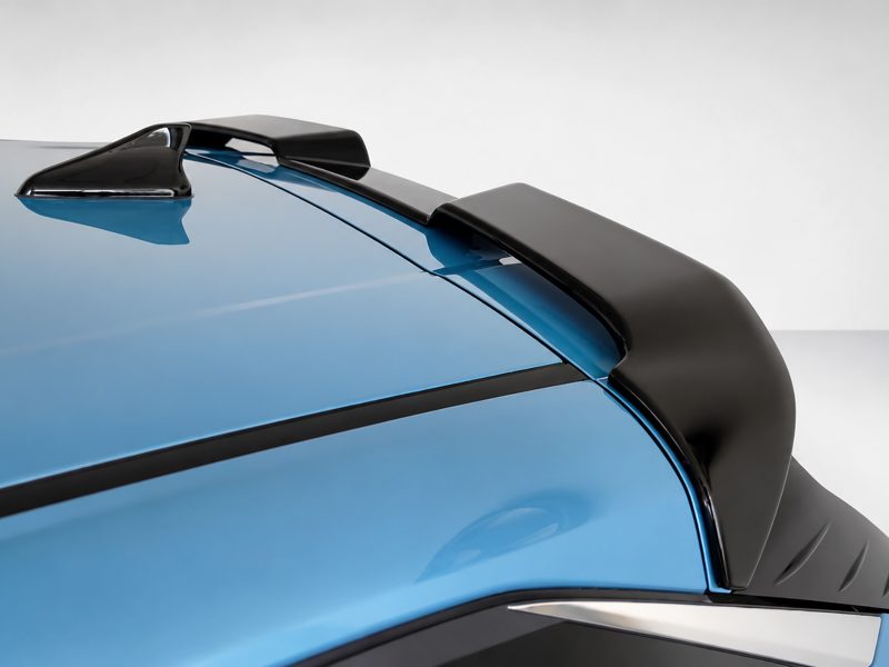 Close-up of a blue car’s rear spoiler and aero edge, highlighting the glossy black wing against a light backdrop.