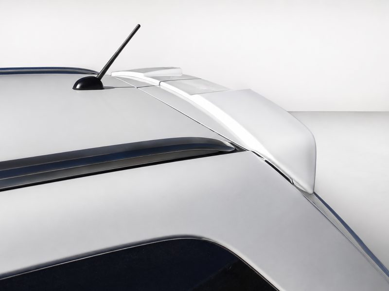 Close-up of a silver car roof showing a black antenna and rear spoiler on a white background.