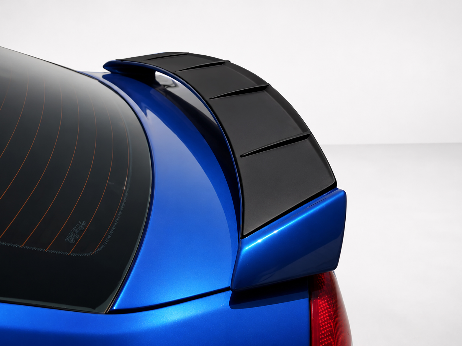 A-469_1jpg - OPSHOLDERS Close-up of a blue hatchback rear with a black spoiler and rear window defroster lines visible on the glass.
