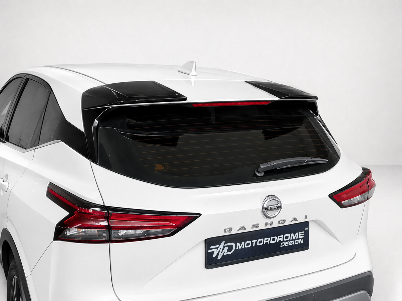 A-471_1jpg - OPSHOLDERS White Nissan SUV rear view with black roof spoiler, tinted rear window, and red taillights; Nissan badge visible above the Motordrome Design plate.