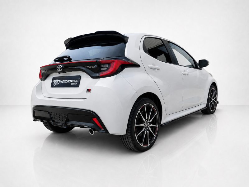 A-474_3-1jpg - OPSHOLDERS Rear three-quarter view of a white Toyota hybrid hatchback with black roof spoiler and large black alloy wheels in a studio setting.