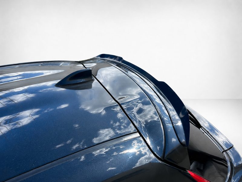 Close-up of a glossy blue car roof with a shark-fin antenna and curved panels reflecting clouds against a light background.