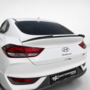 Rear-left view of a white Hyundai hatchback with dark-tinted rear window, prominent taillights, and spoiler in a studio setting