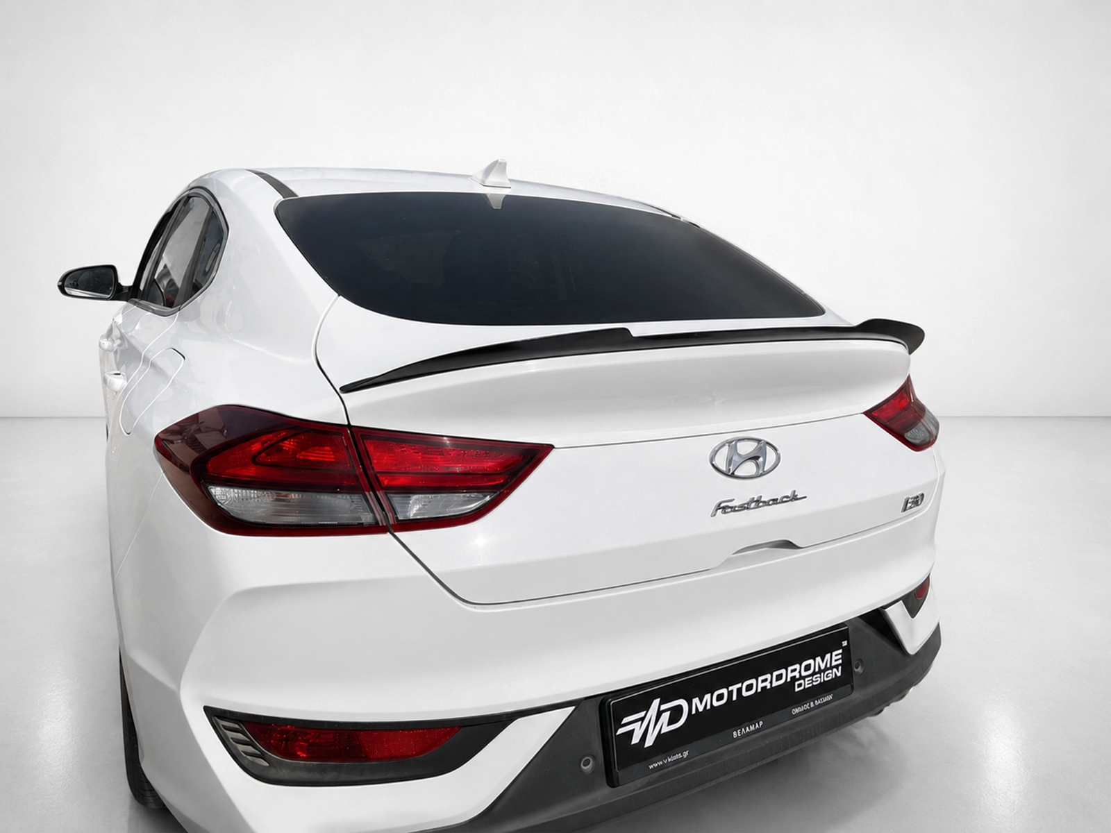 A-477_1jpg - OPSHOLDERS Rear-left view of a white Hyundai hatchback with dark-tinted rear window, prominent taillights, and spoiler in a studio setting