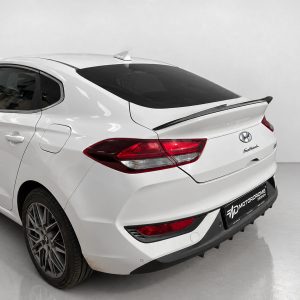 A-477_4jpg - OPSHOLDERS Rear three-quarter view of a white Hyundai sedan with a spoiler, in a studio setting with tinted rear window and alloy wheels.