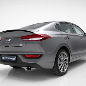 Gray Hyundai i30 Fastback viewed from rear-left in a white studio, with rear spoiler and exhaust visible.