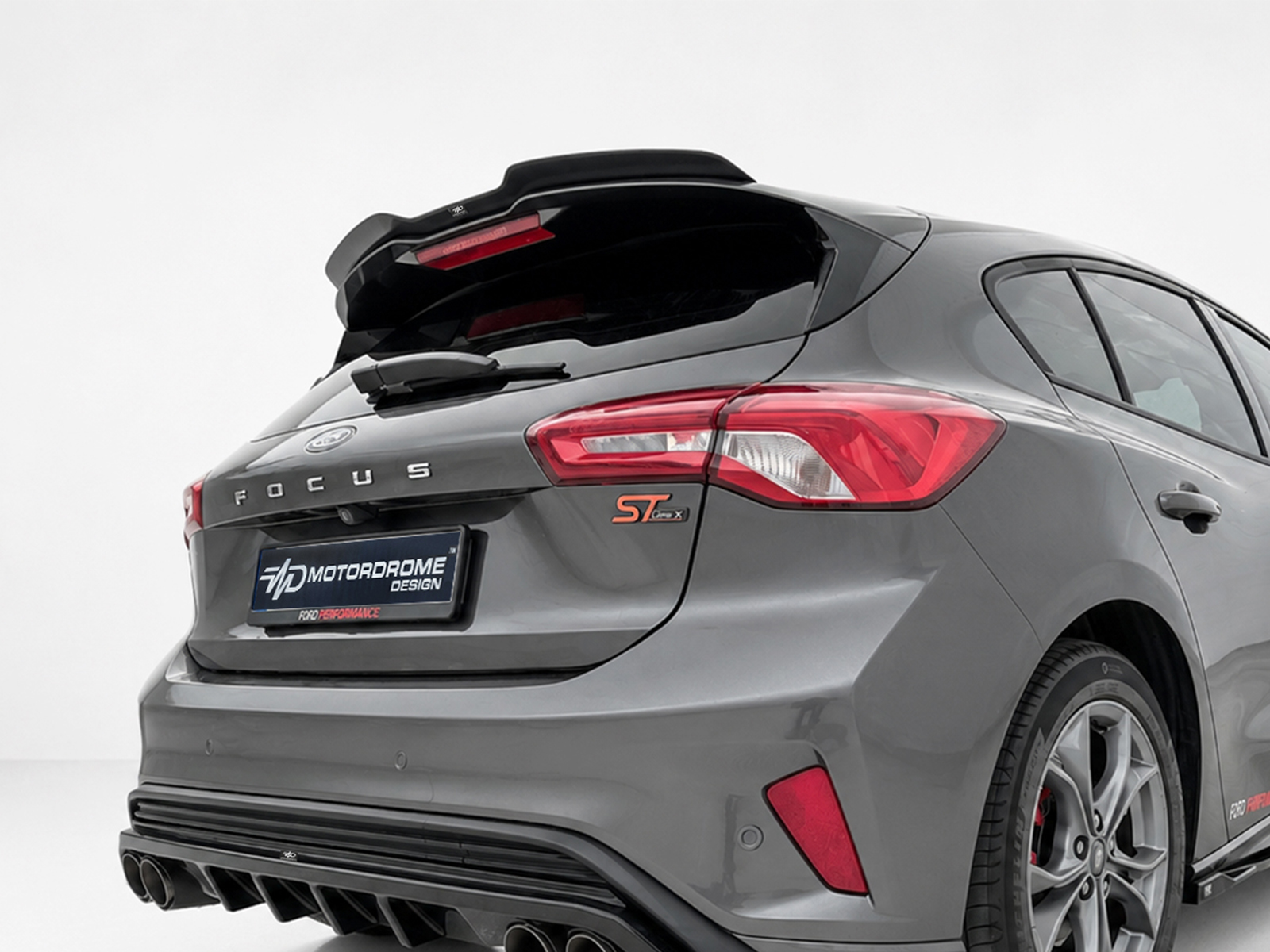 A-479_1jpg - OPSHOLDERS Rear view of a gray Ford Focus hatchback with sporty ST badge, showing large rear spoiler and dual exhausts