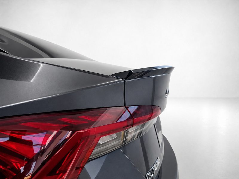 Rear view of a dark gray car showing a spoiler and red taillight assembly in the trunk area.