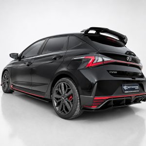 Rear three-quarter view of a black Hyundai hatchback with red accent trim, sporty body kit, and roof spoiler in a studio setting.