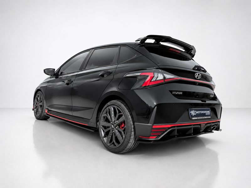 Rear three-quarter view of a black Hyundai hatchback with red accent trim, sporty body kit, and roof spoiler in a studio setting.