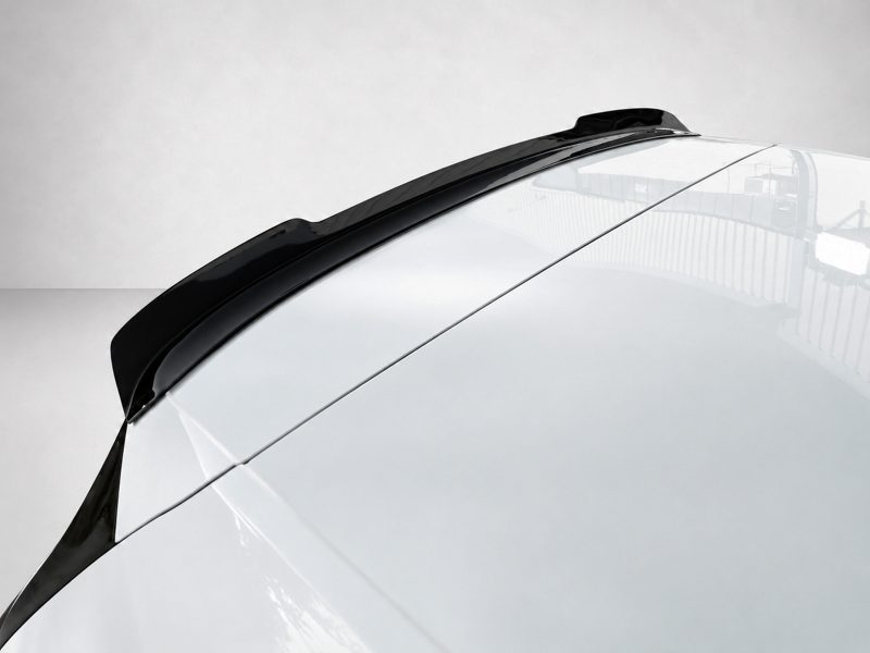 Close-up of a white car roof with a black rear roof spoiler along the edge, reflecting light on a clean surface.