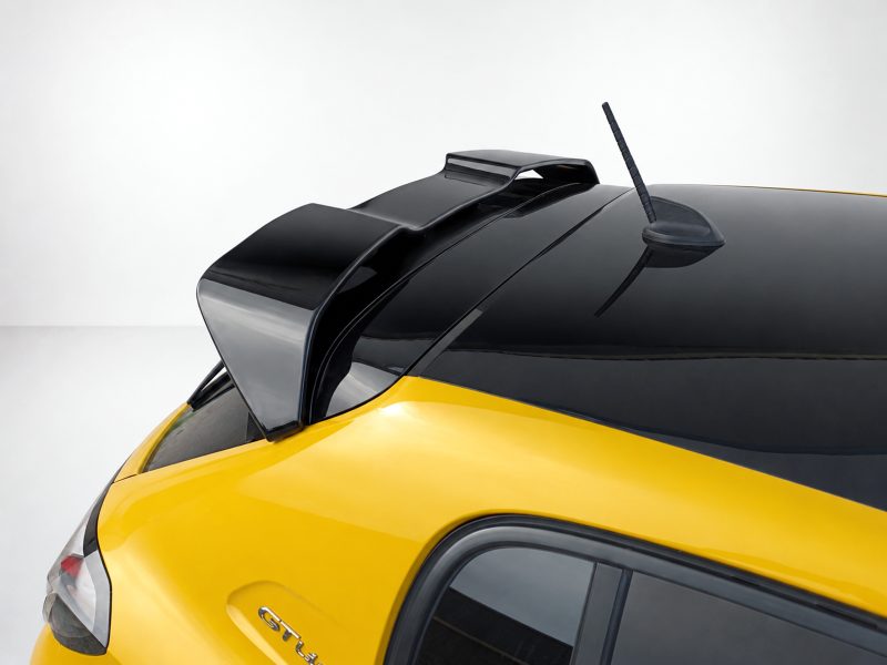 Yellow car with black roof, showing a raised rear spoiler and antenna, viewed from the rear passenger side