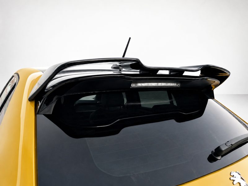 Yellow car seen from above focusing on the black roof spoiler and rear window, with a rooftop antenna visible.