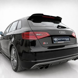 A-487_2jpg - OPSHOLDERS Rear view of a black Audi S3 Sportback in a studio, featuring red taillights, a subtle roof spoiler, and quad exhausts.