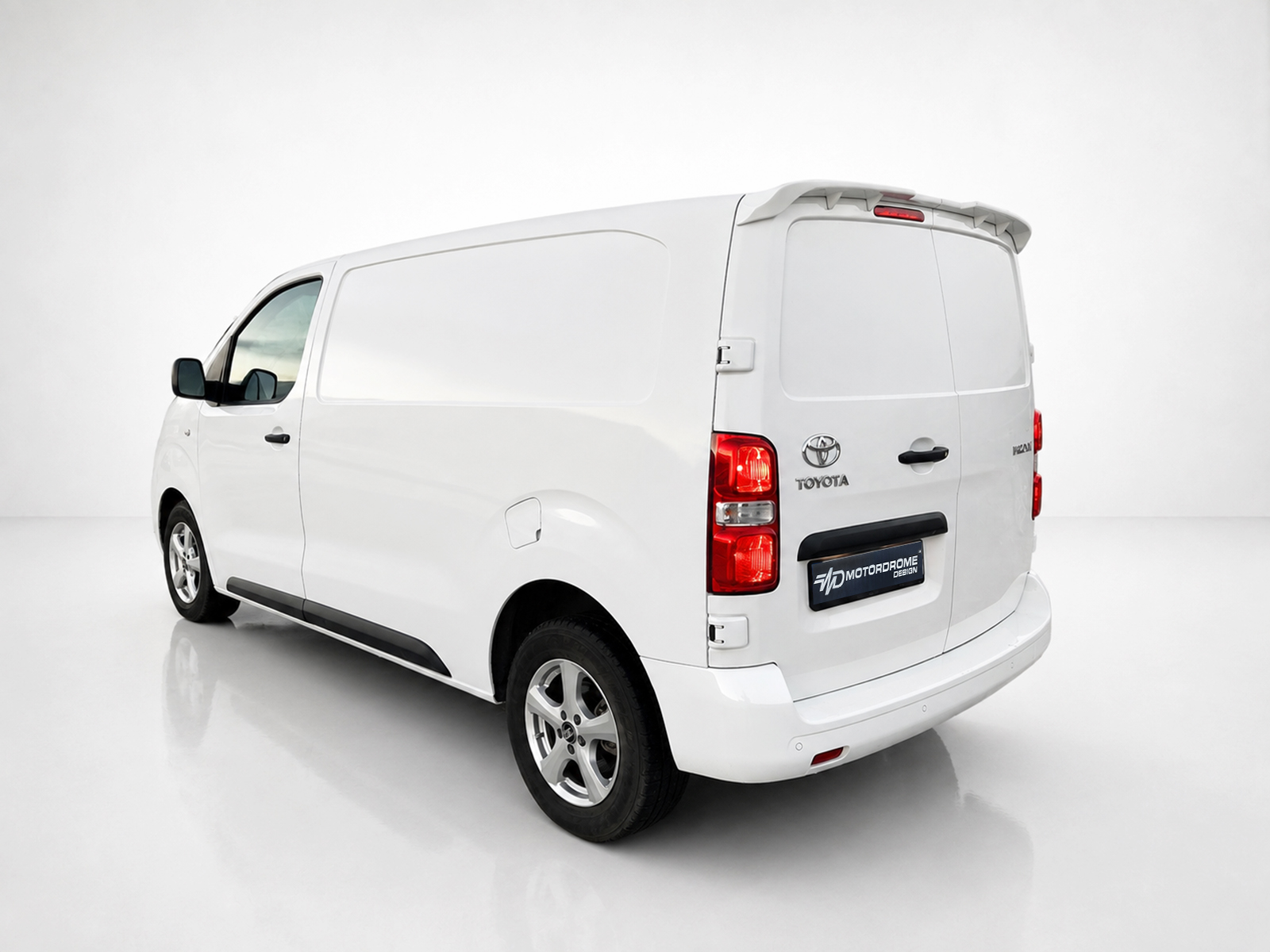A-488_2jpg - OPSHOLDERS White cargo van shown from a rear-left angle in a studio setting with clean reflective floor. The back doors and taillights are visible.