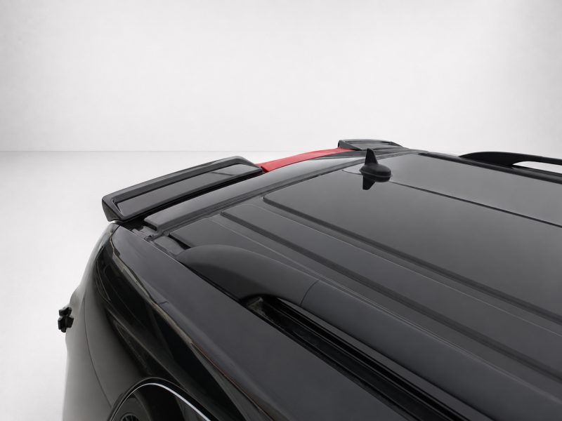 Close-up of a black car roof with a rear spoiler, shark-fin antenna, and red highlight against a light background.