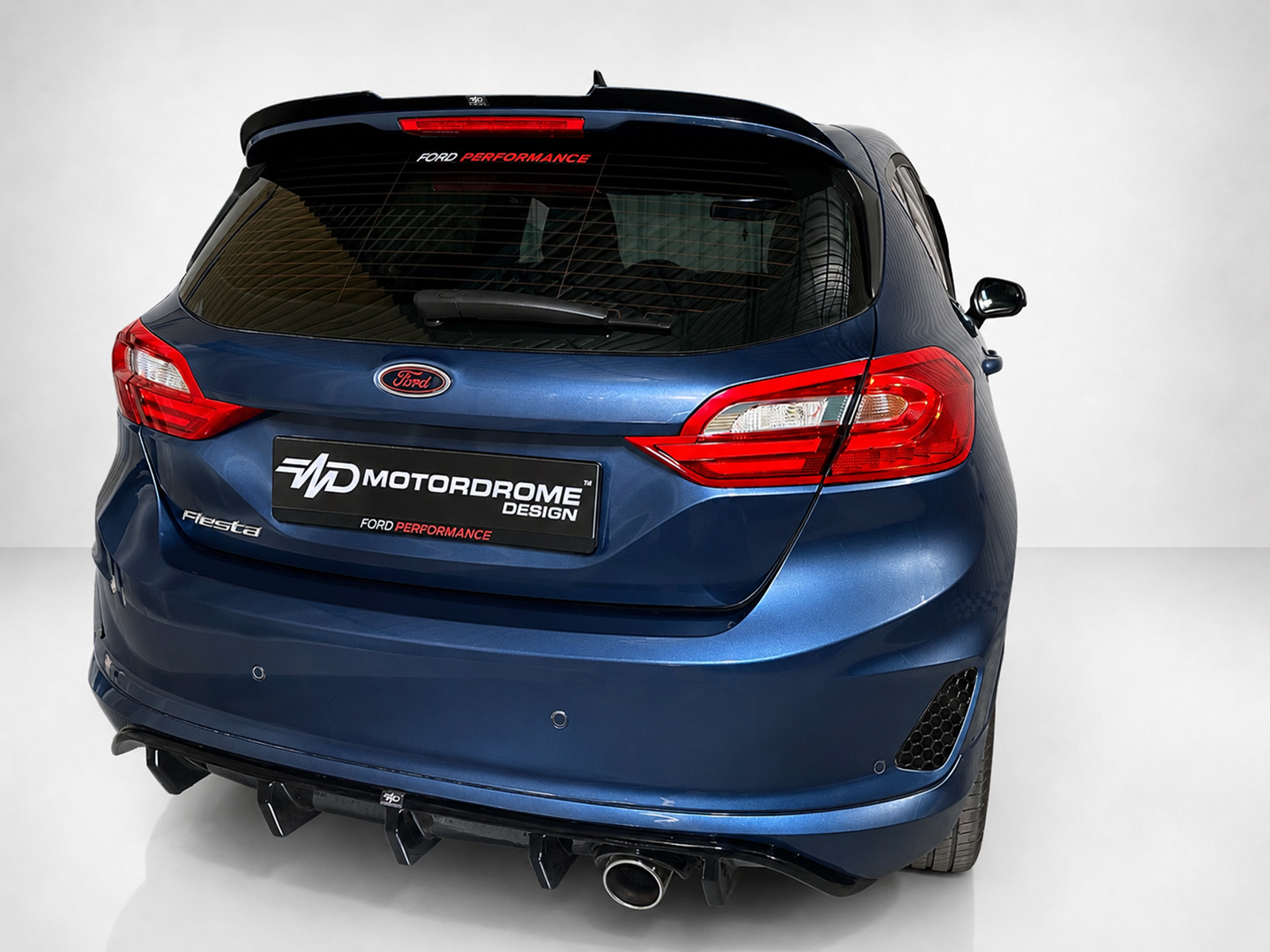 A-493_2jpg - OPSHOLDERS Blue Ford hatchback rear view with Motordrome Design plate and red taillights.