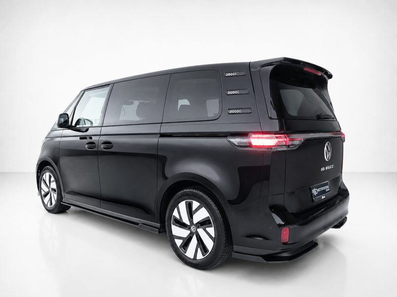 Black Volkswagen ID. Buzz electric van, rear-left three-quarter view in a white studio, taillights illuminated.