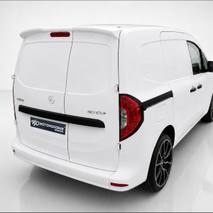 White cargo van viewed from the rear-right, showing back doors, red taillights, and a black rear bumper with a MotorDome Design sticker on the tailgate.