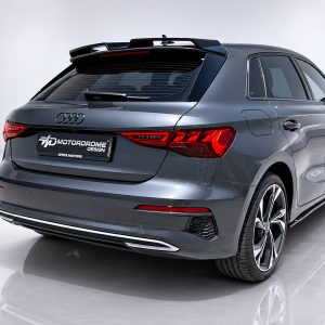 Rear three-quarter view of a metallic gray Audi SUV in a studio, showing taillights, rear hatch, and large alloy wheels with a branded license plate area.