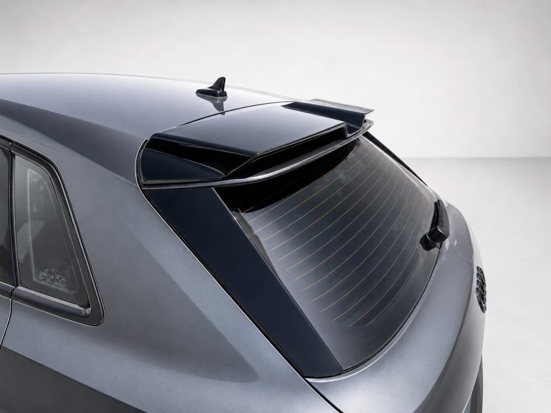 Rear view of a gray hatchback car showing a roof spoiler and rear window with defroster lines.