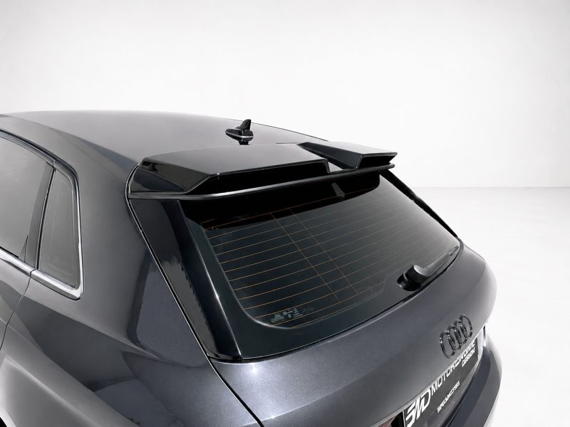 Rear view of a dark gray Audi SUV with a roof spoiler and rear wiper on a light background.