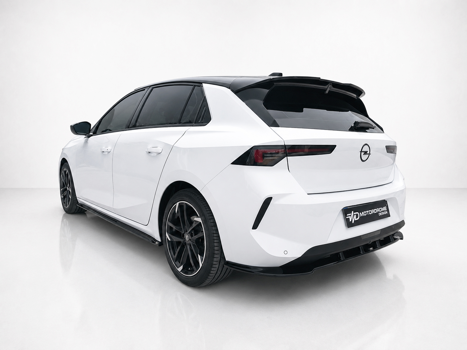 A-501_2jpg - OPSHOLDERS Rear three-quarter view of a white Opel hatchback in a studio, with a black roof spoiler and dark alloy wheels on display.