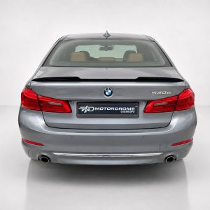 Rear view of a gray BMW 530e in a studio, showing the trunk, taillights, and a Motordrome Design plateplate on the bumper.