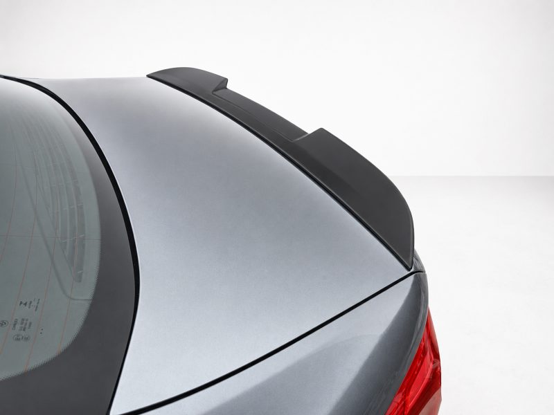 Close-up of a car's rear trunk with a black aerodynamic spoiler on a silver vehicle rear lid, taillight visible at the edge